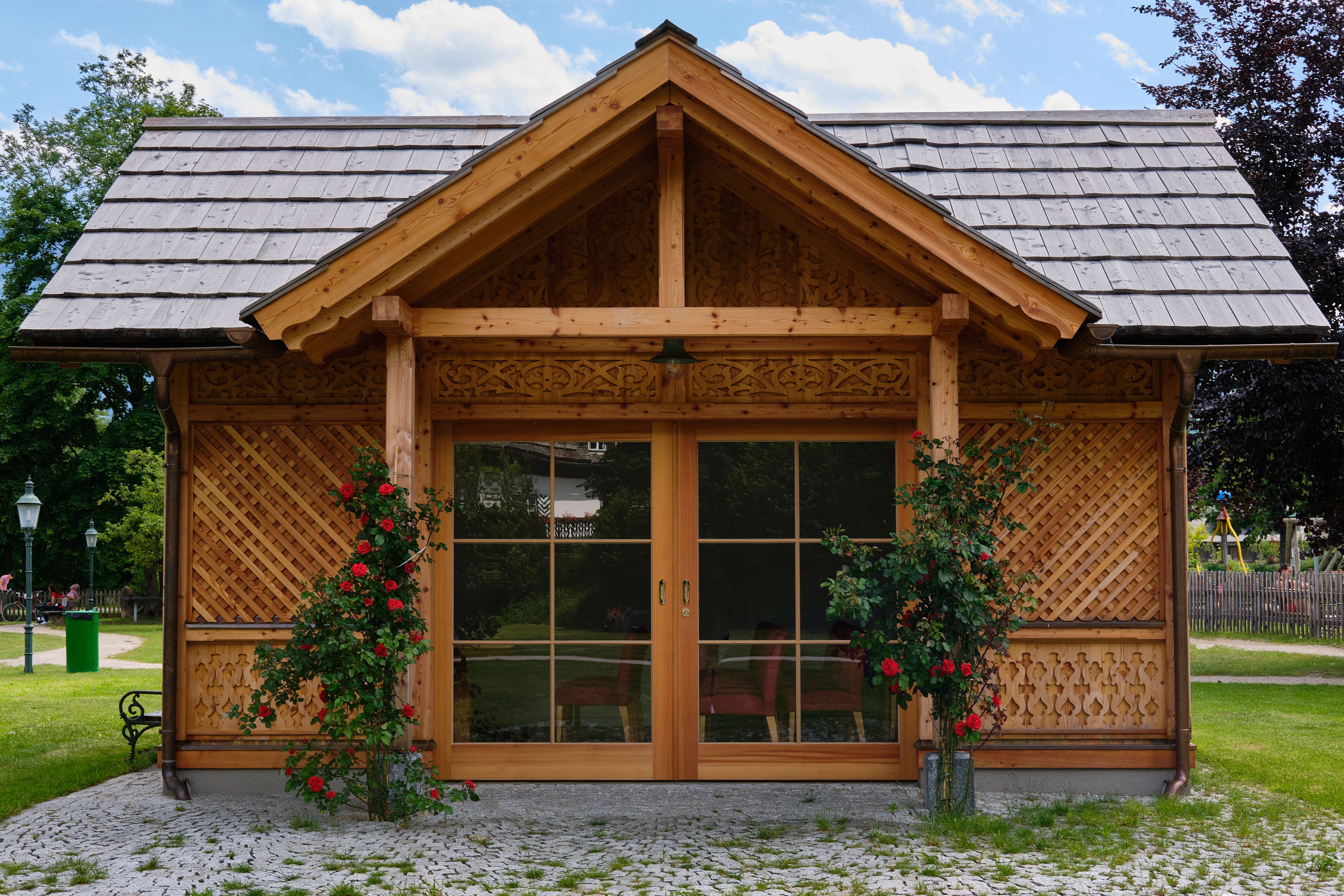 Beautiful wooden bungalow with glass doors and red roses in a lush garden setting.
